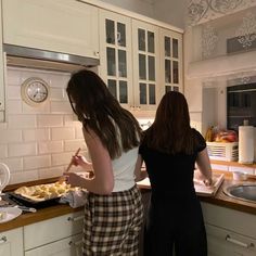 two women standing in a kitchen preparing food on top of a counter next to each other