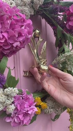 a person holding a gold bird shaped object in front of purple and white flowers