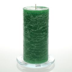 a green candle sitting on top of a glass stand with a white background behind it