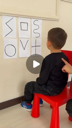 a little boy sitting on top of a red chair in front of a white wall