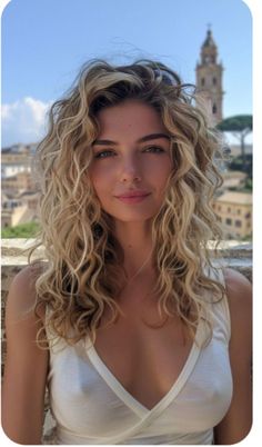 a woman with long curly hair standing in front of a clock tower and looking at the camera