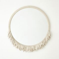 a circular mirror with white feathers hanging on it