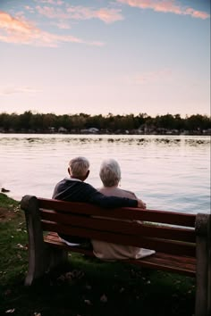 an older couple sitting on a bench looking out over the water at sunset or sunrise