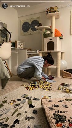 a woman kneeling down on the floor in front of a cat tree and playing with toys