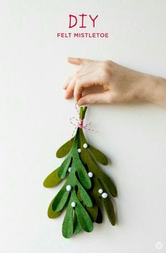 a hand is holding a felt mistlete ornament on a white wall