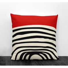 a red and black pillow sitting on top of a wooden floor next to a white wall