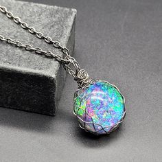 Embrace the mystery of the universe with this round galaxy cabochon set in braided darkened steel! It is totally handmade, with unique original design. The double sided pendant features amazing iridescent sparkling colors that opalesce and bot refracts and light to show a rainbow nebula on one side and a black backed cabochon.  It is made with heat darkened steel, using man-made cabochons instead of mined gems, so it is very environmentally friendly. Handmade Iridescent Necklace With Round Pendant, Mystical Metal Round Pendant Jewelry, Mystical Round Pendant Metal Jewelry, Iridescent Mystical Pendant Jewelry, Mystical Iridescent Pendant Jewelry, Unique Stainless Steel Round Pendant Jewelry, Unique Stainless Steel Round Pendant, Mystical Round Cabochon Jewelry, Handmade Iridescent Magical Jewelry