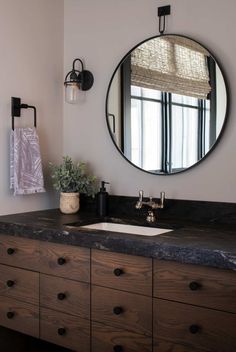 a bathroom sink with a round mirror above it and wooden drawers underneath the countertop