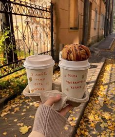 two coffee cups with cinnamon rolls in them are held up by someone's hand