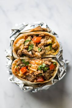 two burritos sitting on top of foil covered in meat and veggies