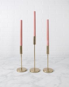 two pink candles sitting on top of each other in front of a white brick wall