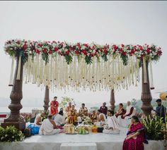 a group of people sitting on top of a white table under a flower covered canopy