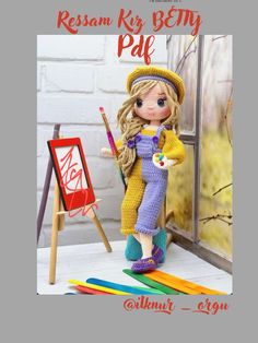 the doll is holding a paintbrush in her hand and standing next to an easel