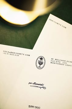 two envelopes sitting next to each other on top of a green table with a gold spoon in the background