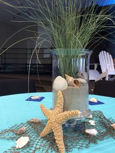 there is a starfish on the table next to a glass vase with sea shells