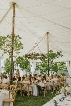 a group of people sitting at tables under a tent with white linens on it