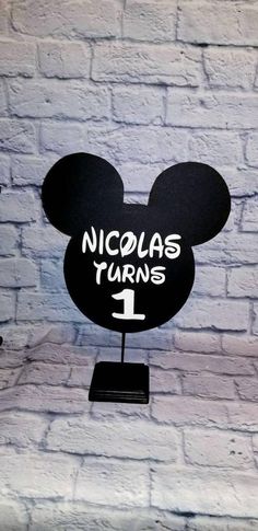 a mickey mouse head with the words nicholas turns 1 on it's face and is standing in front of a brick wall