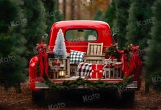 an old red truck decorated for christmas with presents and trees in the back seat is surrounded by evergreens