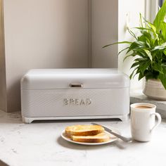 a white toaster sitting on top of a counter next to a cup of coffee