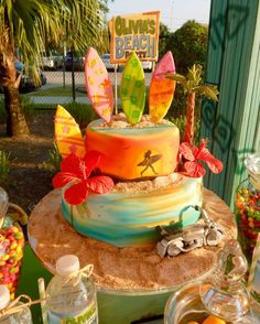 there is a colorful cake with surfboards on it and candy in the bottom tier