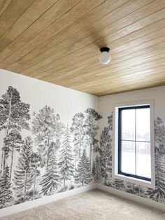 an empty room with trees painted on the wall and a window in the corner,