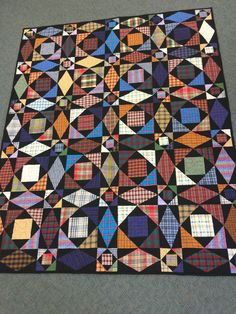 a black quilt with multicolored squares on the top and bottom is laying on carpet