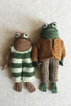 two knitted frog dolls sitting next to each other on top of a white surface