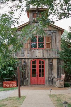 an old barn with a red door and sign in the foreground that says the barn