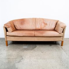 a tan leather couch sitting on top of a cement floor next to a white wall