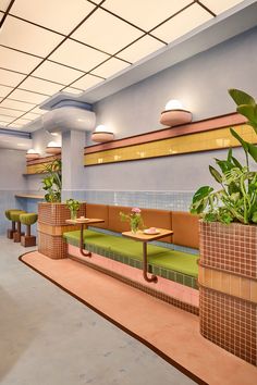 the interior of a restaurant with potted plants on benches and tables in front of them