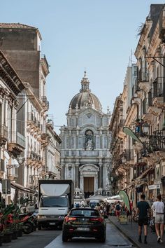 cars and people walking on the street in front of an old building with a dome