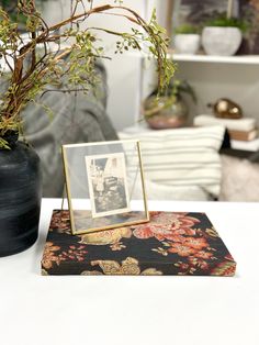 a vase with some plants in it sitting on a table next to a photo frame