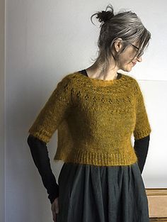 a woman standing in front of a dresser wearing a yellow sweater and black skirt with her hands on her hips