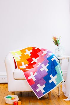 a white couch with a multicolored blanket on top of it next to a potted plant