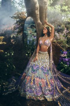 A blue lehenga set adorns an embroidered forest setting using glass cut crystals, gold metal embellishments, and applieques of rich organzas and tissue. This is paired with our rose bralette embrodiered in shades of multi-colour glass cut beads, with a shoulder attached delicate tulle dupatta trail embroidered in gold metal embellishments. DELIVERY TIMEPlease wait 8-12 weeks for your outfit to arrive. FABRIC DETAILSTulle, Organza Professional cleaning only. Purple Forest, Purple Lehenga, Baju Kahwin, Forest Setting, Metal Embellishments, Traditional Indian Dress, Blue Lehenga, Embroidered Lehenga, Indian Dresses Traditional