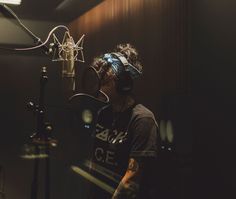 a man with headphones on in front of a microphone and recording equipment behind him