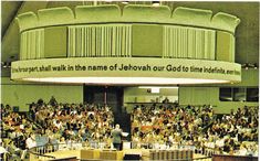 an auditorium full of people sitting and standing in front of a podium with a sign that reads, we shall walk in the name of jehovan our god to find time