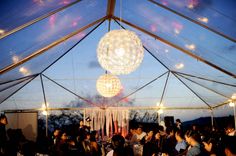 a group of people sitting under a tent with lights hanging from it's ceiling