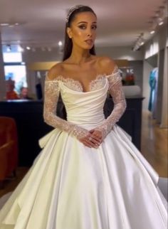 a woman wearing a white wedding dress with long sleeves and an off the shoulder top