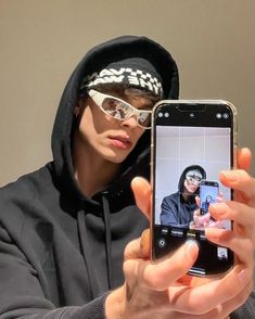 a person in a hoodie holding up a cell phone to take a selfie