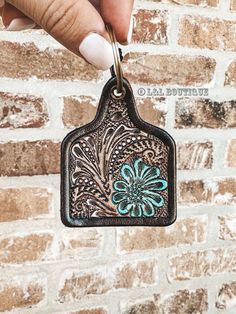 a hand holding a keychain with a flower on it in front of a brick wall