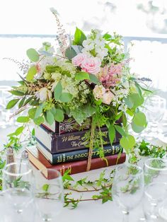 a stack of books sitting on top of a table covered in flowers and greenery