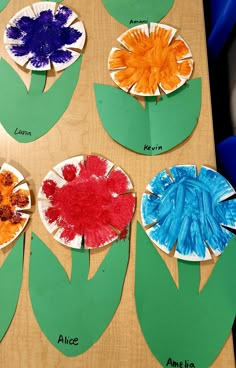 paper plates with flowers on them sitting on top of a wooden table next to green leaves