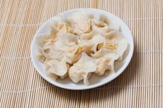 a white bowl filled with dumplings sitting on top of a bamboo tablecloth covered floor