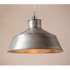 a large metal light hanging from a ceiling fixture in a room with brick wall behind it