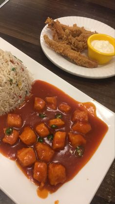 a plate with rice, meat and sauce on it next to another plate filled with food