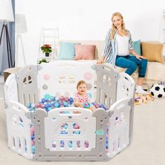 a woman sitting on a couch next to a child's playpen with balls in it