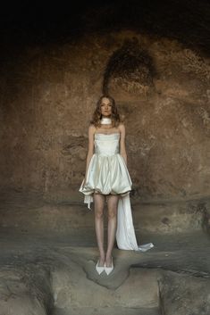 a woman standing in front of a rock formation wearing a white dress and high heels