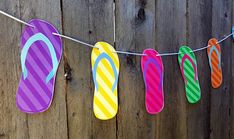 colorful flip flops are hung on a line with clothes pins attached to it, hanging from a wooden fence