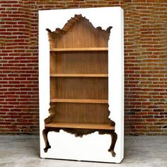 a wooden book shelf sitting on top of a white floor next to a brick wall